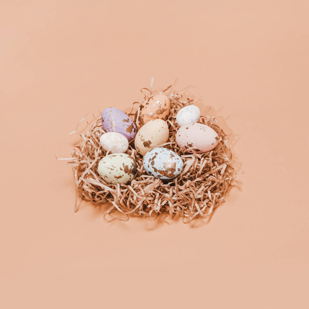 Jednoduchá koncepce jara a Velikonoc. Pár velikonočních barevných vajec v jasném hnízdě. Vejce mají různou velikost a jsou zdobena zlatou strukturou. Minimální složení. Světlé pastelové pozadí. - Fotografie, Obrázek