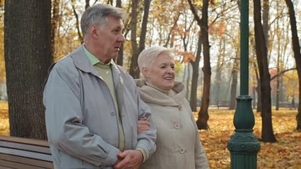 Happy caucasian family walking in autumn park together enjoy free time outdoors mature aged smiling man and woman communicate talking active recreation of elderly couple romance relationships concept - Footage, Video
