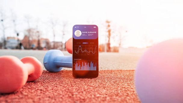 Health app. Smart phone screen with fitness health or sport gym mobile application on dumbbell background. Home online workout - 写真・画像