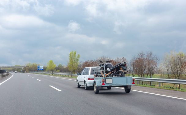 Weißes Auto fährt auf Autobahn mit Anhänger mit Motorrad.  - Foto, Bild