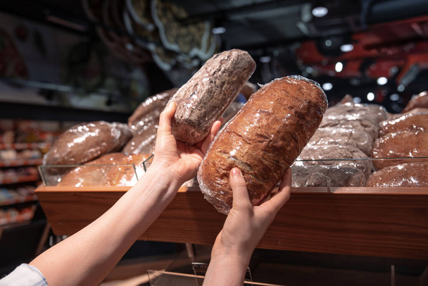 Een vrouw houdt brood in haar handen bij de supermarkt toonbank. - Foto, afbeelding