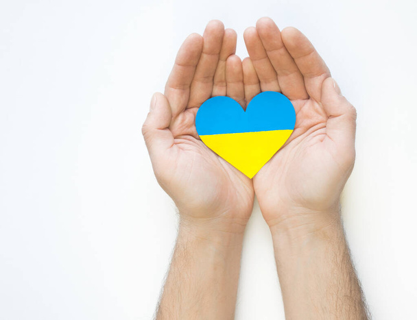 El concepto de amor por Ucrania. corazón en los colores de la bandera de Ucrania en las manos de los hombres sobre un fondo blanco. - Foto, Imagen