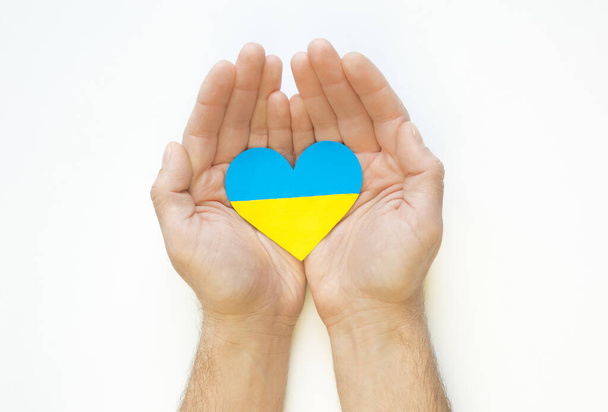The concept of love for Ukraine. Heart in the colors of the flag of Ukraine in men's hands on a white background. - Photo, Image