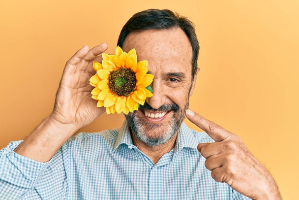 Středověký hispánský muž drží slunečnici přes oko s úsměvem šťastný ukazující rukou a prstem  - Fotografie, Obrázek
