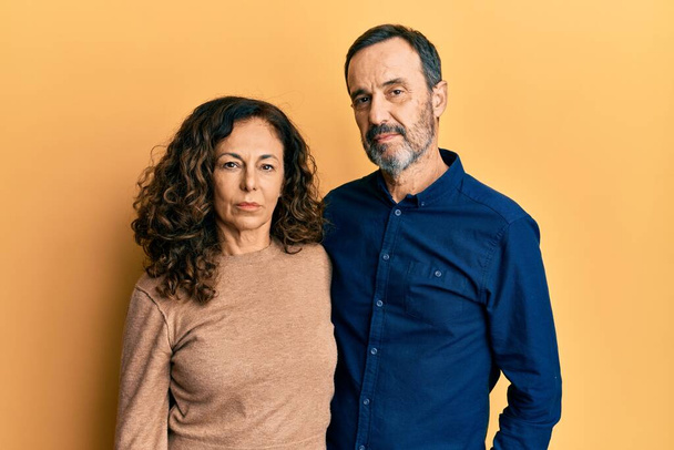Hispánský pár středního věku, oblečený v neformálním oblečení, se uvolnil s vážným výrazem ve tváři. jednoduchý a přirozený pohled do kamery.  - Fotografie, Obrázek