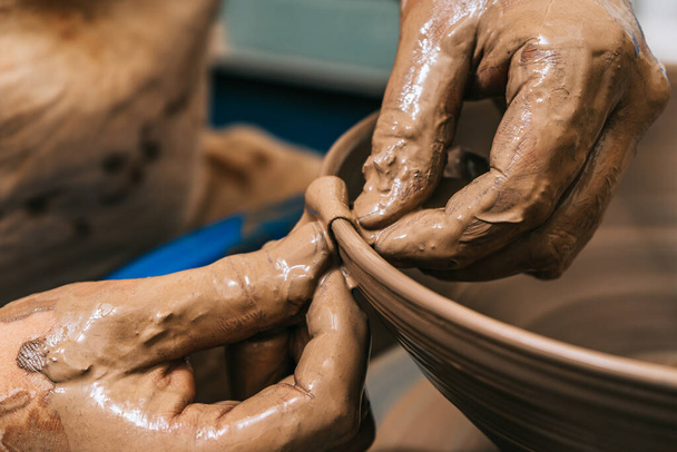 Le mani esperte di un vasaio che lavora l'argilla sulla ruota di un vasaio. L'argilla prende la forma che il vasaio gli dà con il tono di terracotta dell'argilla. - Foto, immagini
