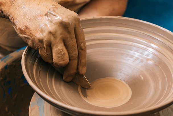 The skilled Hands of a potter working clay on a potter's wheel. The clay takes the shape the potter gives it with the terracotta tone of the clay. - Foto, Imagen