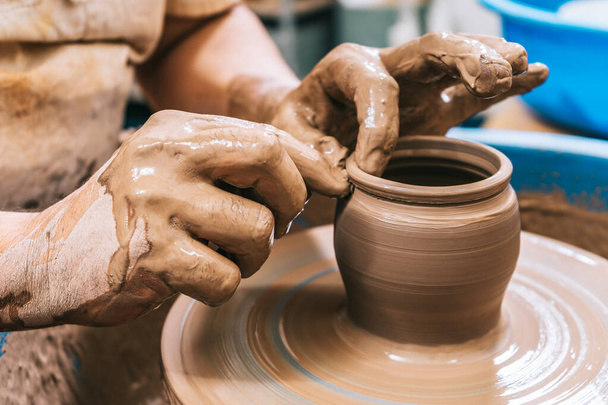 De vaardige handen van een pottenbakker werken klei op een pottenbakkerswiel. De klei neemt de vorm aan die de pottenbakker het geeft met de terracotta toon van de klei. - Foto, afbeelding