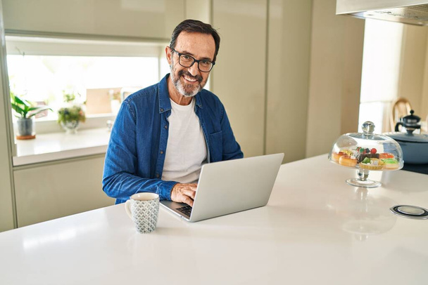 Hombre de mediana edad sonriendo confiado usando el ordenador portátil en casa - Foto, Imagen