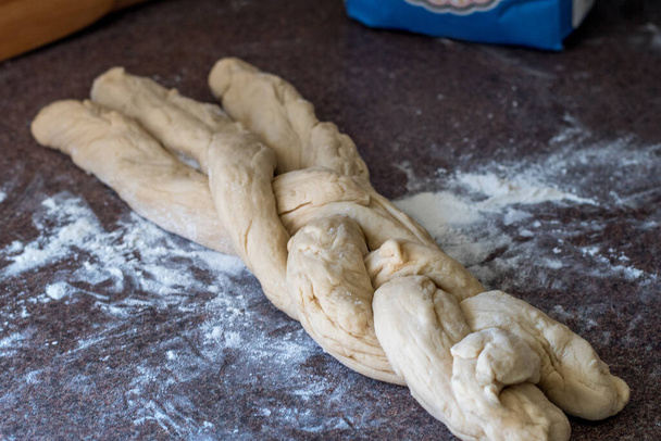 three strips of bread dough are braided into a traditional loaf of challah bread - Foto, Imagen