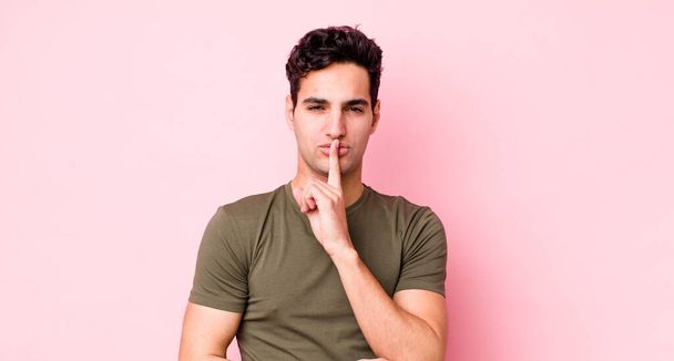 Красивый латиноамериканец выглядит серьезным и прижатым к губам пальцем, требующим тишины или тишины, хранящим секрет - Фото, изображение