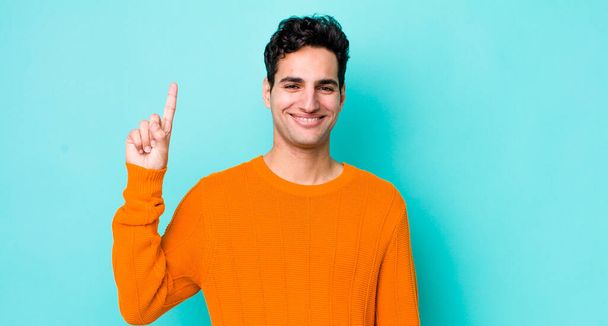 handsome hispanic man smiling cheerfully and happily, pointing upwards with one hand to copy space - 写真・画像