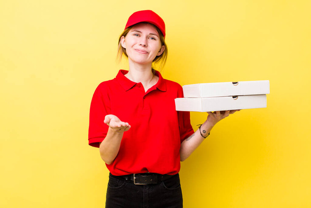 Kızıl saçlı, güzel bir kadın arkadaşça gülümsüyor ve bir konsept sunuyor. Pizza dağıtımı kavramı - Fotoğraf, Görsel