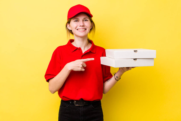 red head pretty woman smiling cheerfully, feeling happy and pointing to the side. delivery pizza concept - Foto, Bild