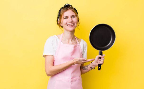 red head pretty woman smiling cheerfully, feeling happy and showing a concept. fry pan and housewife concept - Foto, immagini