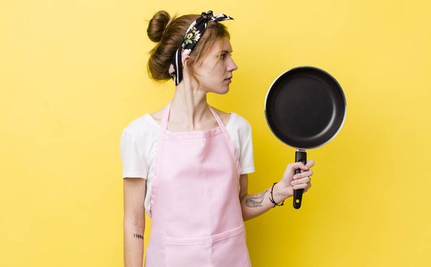 red head pretty woman on profile view thinking, imagining or daydreaming. fry pan and housewife concept - Photo, Image