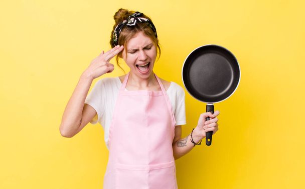 red head pretty woman looking unhappy and stressed, suicide gesture making gun sign. fry pan and housewife concept - Foto, afbeelding