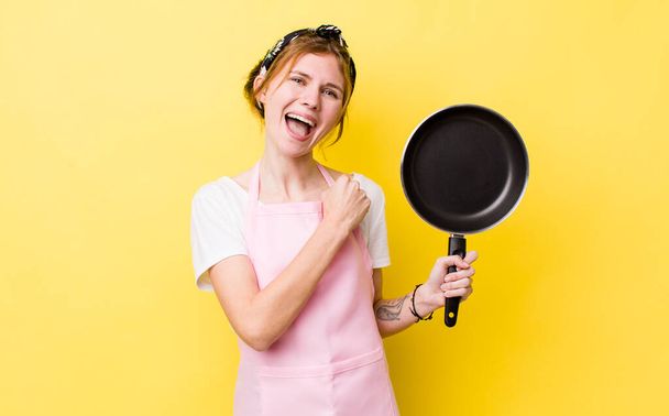 red head pretty woman feeling happy and facing a challenge or celebrating. fry pan and housewife concept - Photo, Image