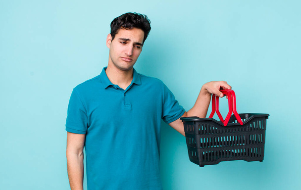 handsome hispanic man feeling sad, upset or angry and looking to the side. shopping basket concept - Foto, Imagem