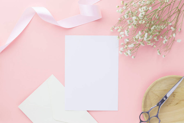 Blank greeting card invitation Mockup 5x7 on envelope with gypsophila flowers and ribbon on pink pastel paper background, flat lay, mockup - Photo, Image