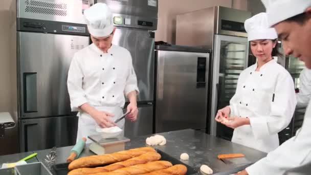 Professionelles Gourmet-Team, vier Köche in weißen Kochuniformen und Schürzen kneten Teig und Eier, bereiten Brot und Backwaren zu, backen im Ofen in der Edelstahl-Restaurantküche. - Filmmaterial, Video
