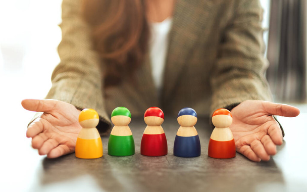 Closeup image of a woman showing a group of different colors wooden people toy in hands for diversity and business concept - Photo, Image