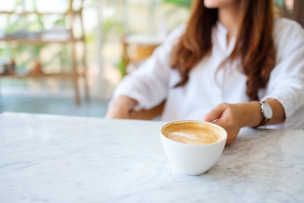 Szoros kép egy nőről, aki egy csésze forró kávét visz az asztalra. - Fotó, kép