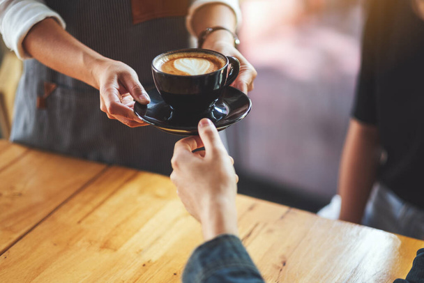 Een serveerster die een kop hete koffie serveert aan een mannelijke klant in café - Foto, afbeelding