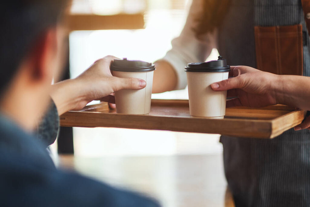 Egy pincérnő, aki egy csésze forró kávét tart és szolgál fel a vendégnek a kávézóban. - Fotó, kép