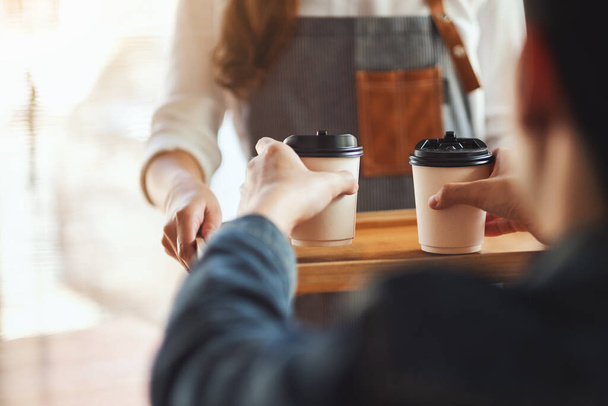 Официантка, держащая и подающая в кафе бумажные чашки горячего кофе - Фото, изображение