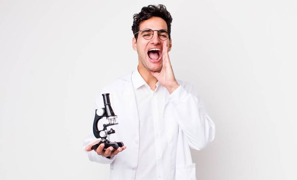 jóképű spanyol férfi boldog, hogy egy nagy kiáltás ki a kezét a száj mellett... tudós mikroszkóp koncepció - Fotó, kép