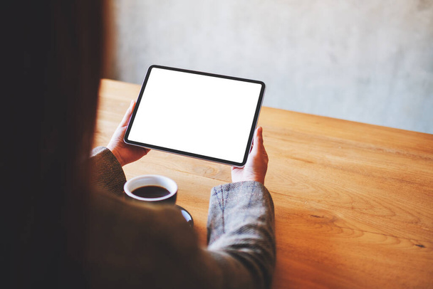 Imagen burlona de una mujer sosteniendo una tableta negra PC con pantalla blanca en blanco con taza de café en la mesa - Foto, imagen