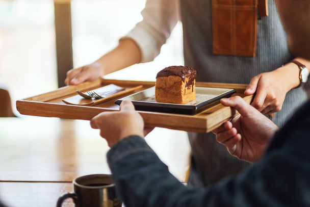 Egy pincérnő kezében és felszolgálása egy darab choux krém az ügyfél a kávézóban - Fotó, kép