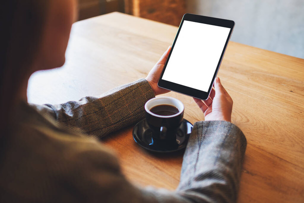 Mockup image of woman holding black tablet pc with blank white screen with coffee cup on wooden table  - Foto, Bild