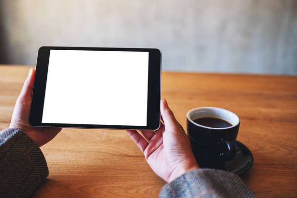 Mockup-Bild der Frau mit schwarzem Tablet-PC mit leerem weißen Bildschirm mit Kaffeetasse auf Holztisch  - Foto, Bild