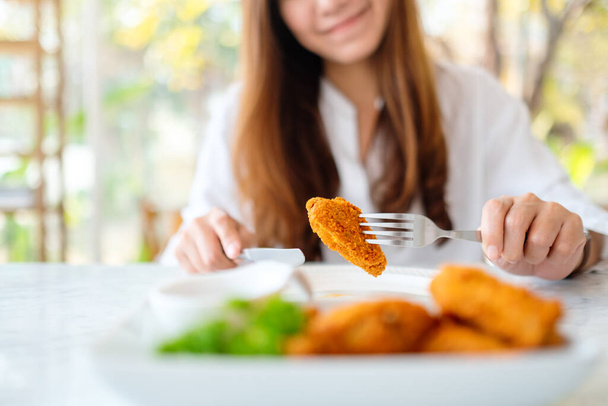 Closeup image of a beautiful asian woman eating fried chicken by fork in restaurant - Foto, Imagem