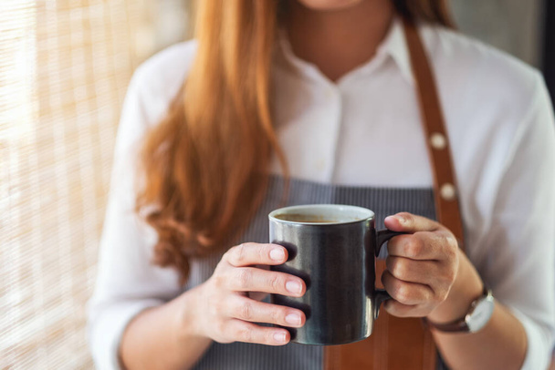 Servírka drží a podává šálek horké kávy v kavárně - Fotografie, Obrázek