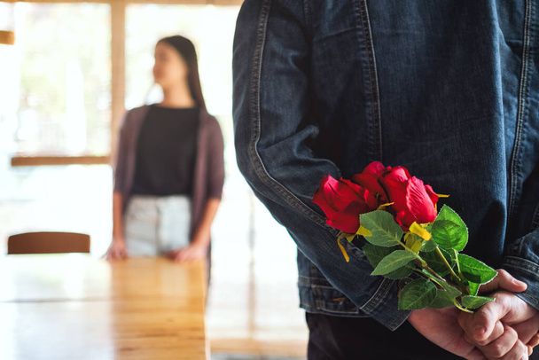 Un hombre sosteniendo y escondiendo el ramo de rosas rojas en su espalda para sorprender a su novia - Foto, Imagen
