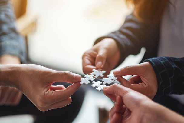 Closeup image of a group of people holding and putting a piece of white jigsaw puzzle together - Photo, Image