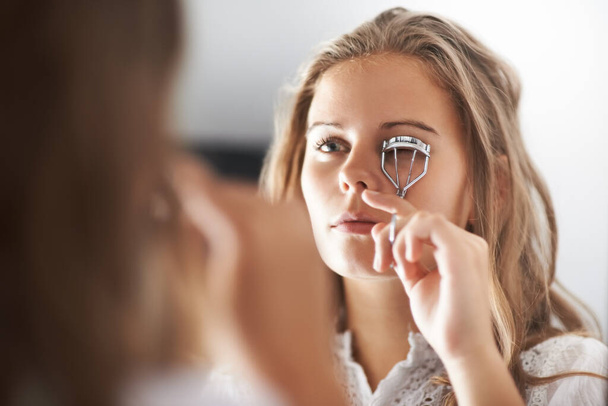 A melhorar a sua beleza natural. Uma adolescente curvando seus cílios no espelho. - Foto, Imagem