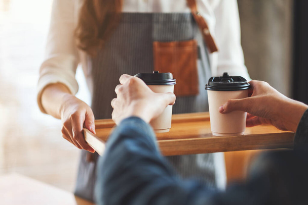 Een serveerster houdt en serveert papieren kopjes hete koffie aan de klant in cafe - Foto, afbeelding