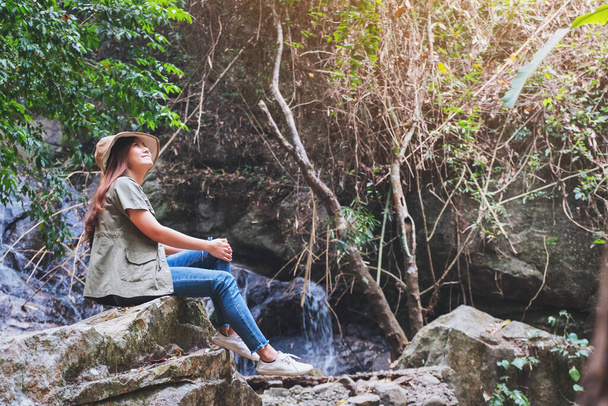 Красивая азиатская женщина сидит на скале перед водопадом - Фото, изображение