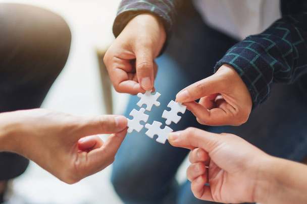 Closeup image of a group of people holding and putting a piece of white jigsaw puzzle together - Photo, Image