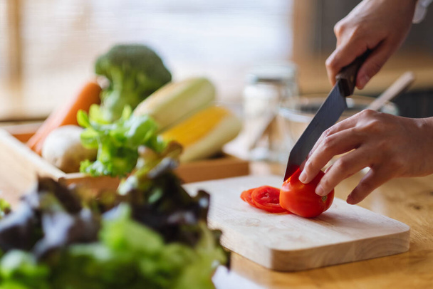 Closeup image of a woman chef cutting and chopping tomato by knife on wooden board - Photo, Image