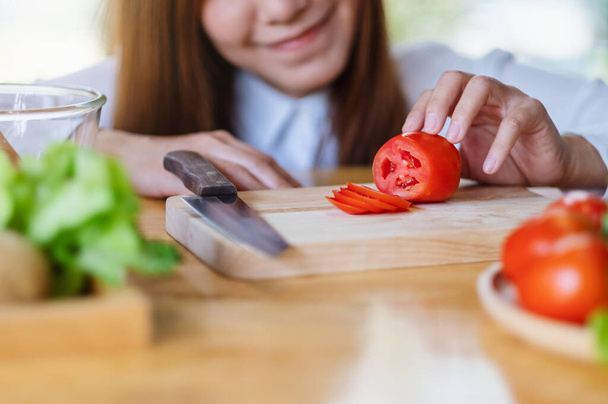 Closeup image of a woman chef looking and cutting tomato by knife on wooden board - Photo, Image