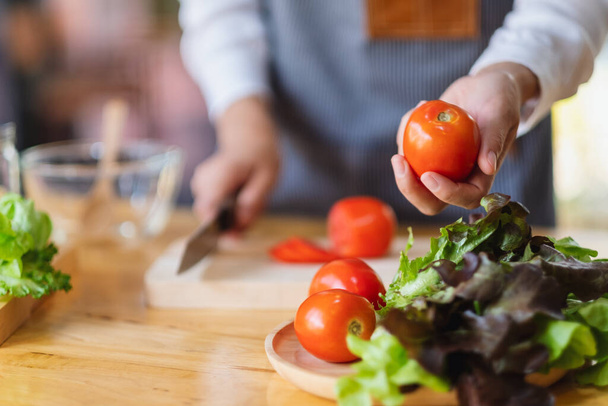 Eine Köchin hält und pflückt eine frische Tomate von einem Gemüsetablett auf dem Tisch - Foto, Bild