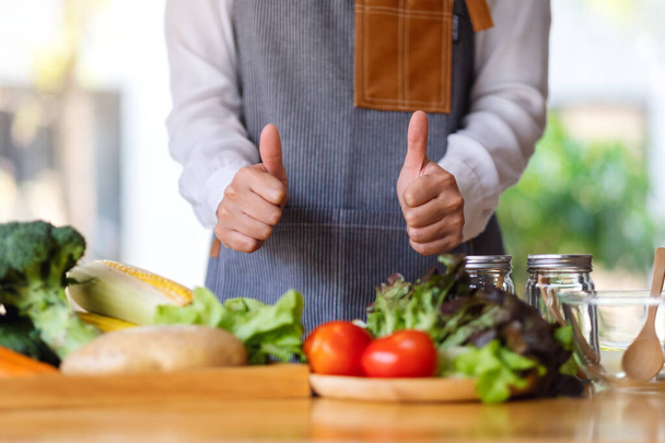 Detailní záběr na ženskou kuchařku, jak dělá a ukazuje palce nahoru rukou znamení při přípravě čerstvé míchané zeleniny vařit v kuchyni - Fotografie, Obrázek