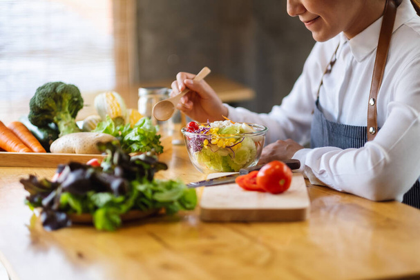 Εικόνα από κοντινό πλάνο μιας σεφ που μαγειρεύει και τρώει φρέσκια σαλάτα ανάμεικτων λαχανικών στην κουζίνα - Φωτογραφία, εικόνα