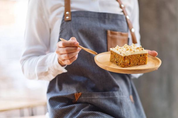 Une cuisinière qui fait cuire et mange un morceau de gâteau à la carotte maison dans un plateau en bois - Photo, image
