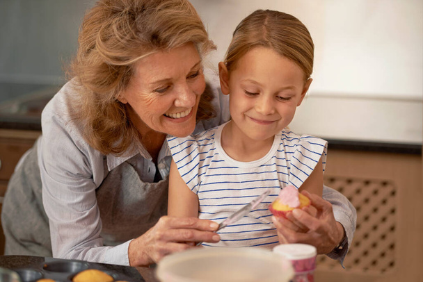 Partager sa sagesse de cupcake. Tournage d'une petite fille décorant des cupcakes avec l'aide de sa grand-mère. - Photo, image